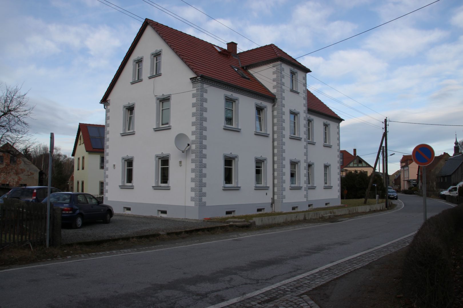 Referenz - Hochbau - Weißes Mehrfamilienhaus in Gaußig an einer Straße mit einem roten Dach und grauen Akzenten