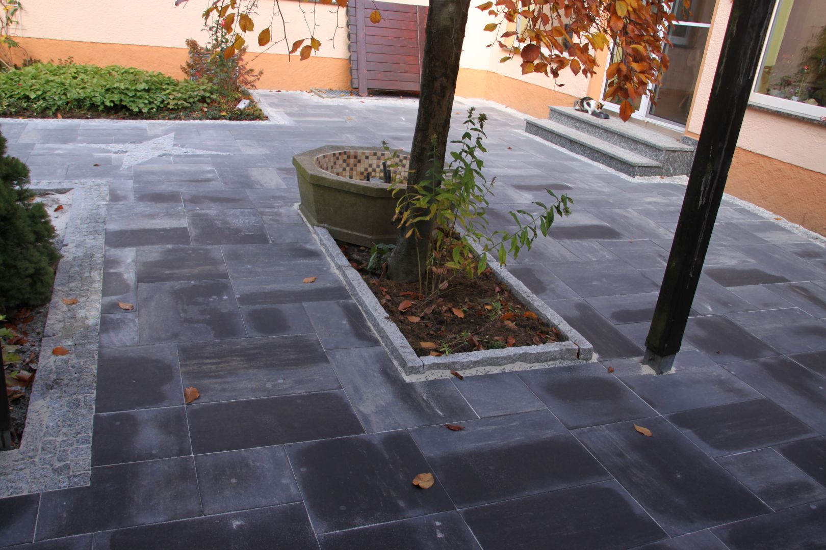 Gepflasterter Hof mit grauen Steinen und Baumumrandungen aus hellem Naturstein, Gartenbau in Bautzen.