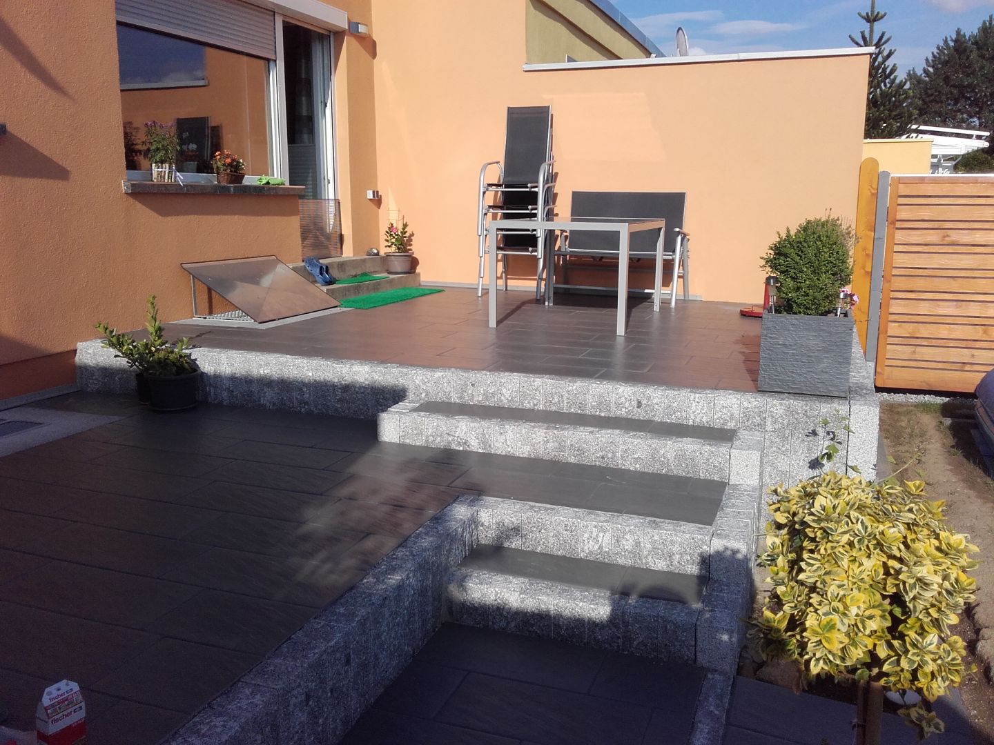 Terrasse mit dunklem Steinpflaster, grauen Natursteinstufen und einer silbernen Sitzgruppe in einer Außenanlage in Bautzen.