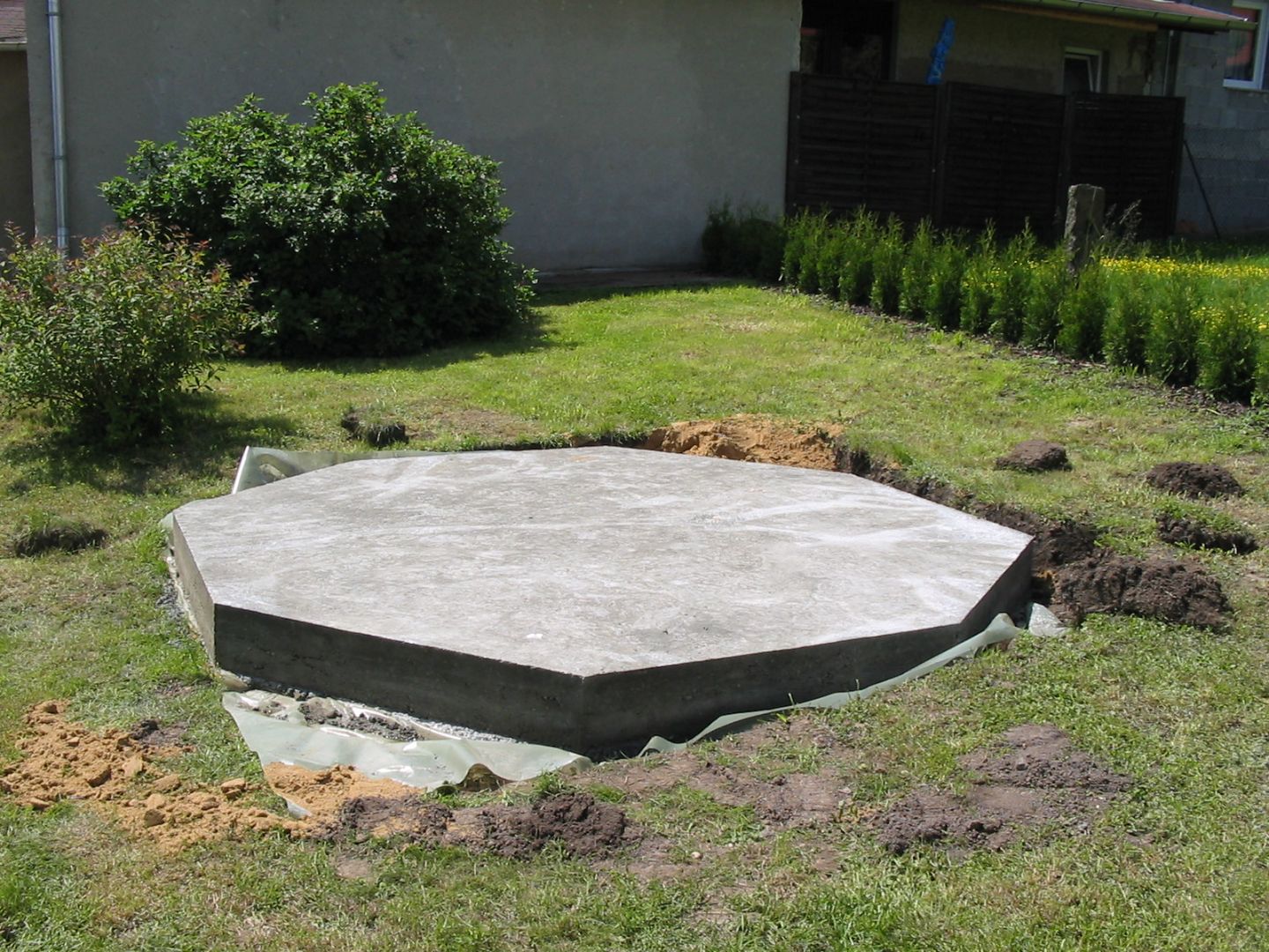 Ein sechseckiges Betonfundament im grünen Garten, vorbereitet für ein Gartenhaus oder eine Kuppel.