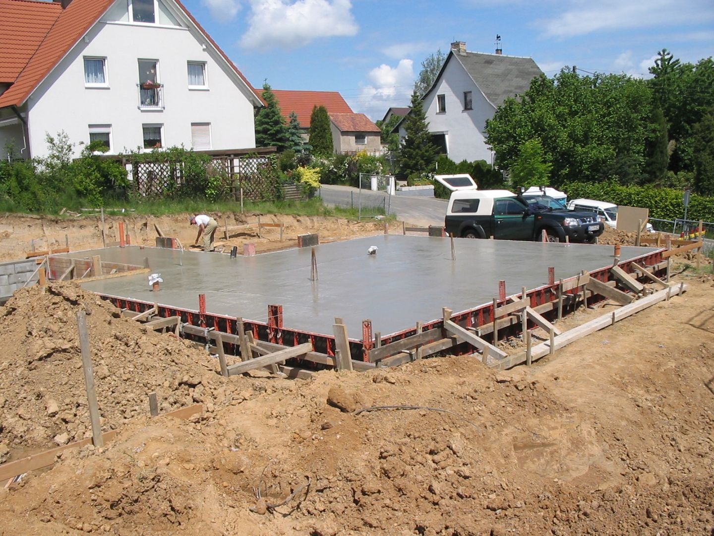 Frisch gegossene Betonbodenplatte für ein neues Haus, mit roter Schalung und einem Arbeiter.